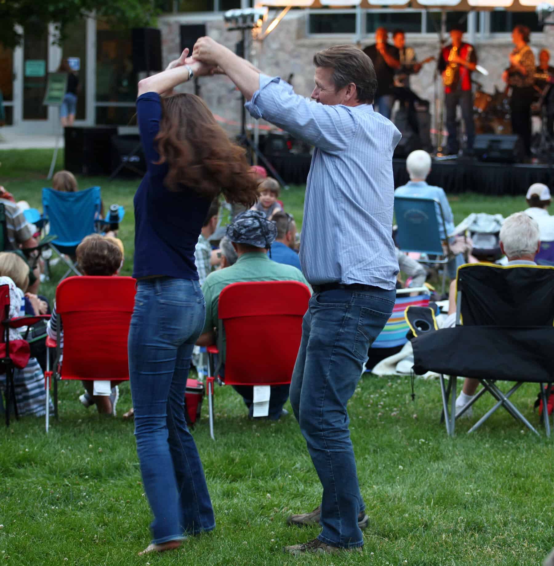 Couple dancing at outdoor concert with audience and band in background.